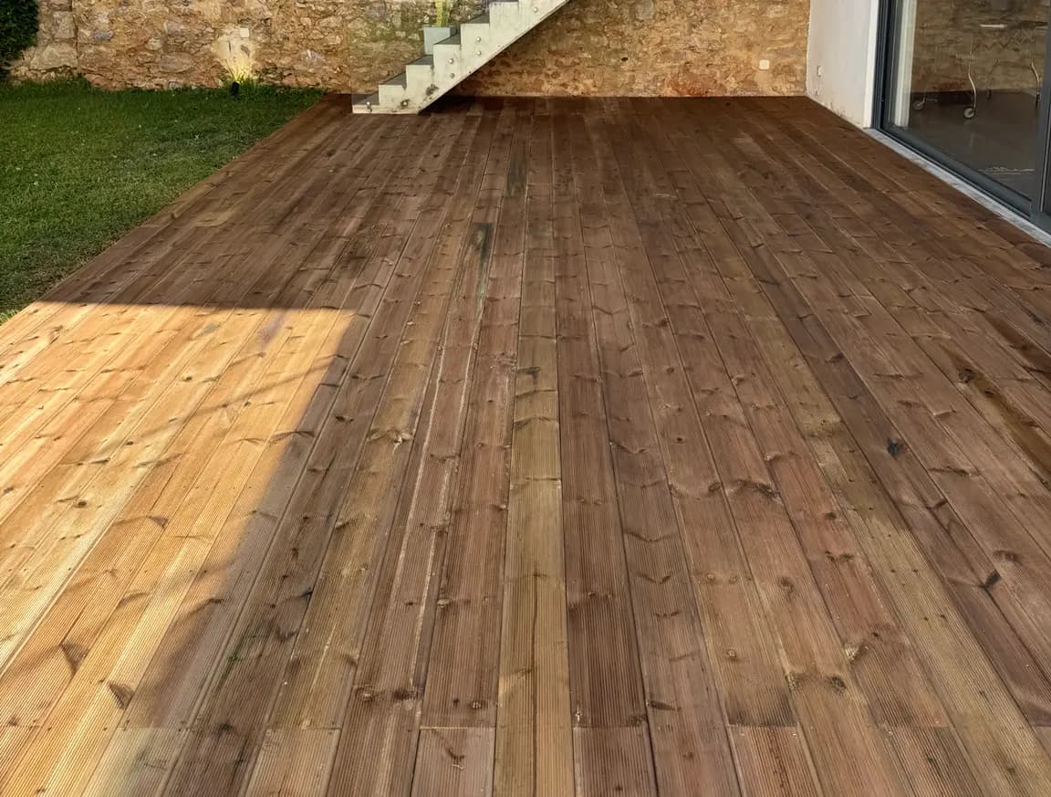 Deck em madeira numa área exterior junto a parede de pedra e escada em vidro, executado pela Arawood Garden.
